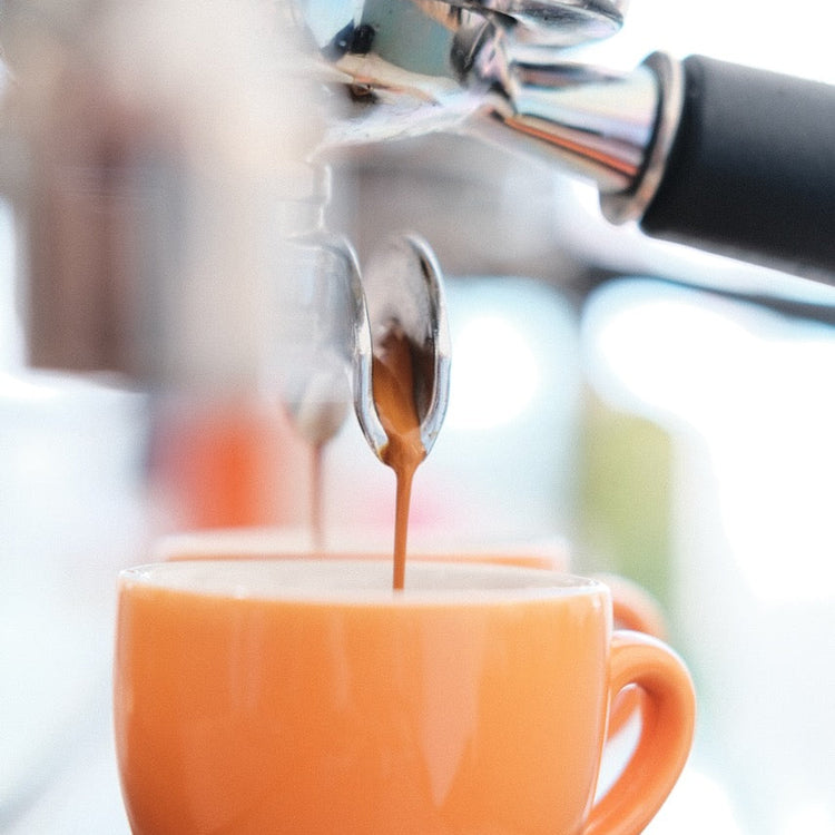 Espresso being poured into an orange mug from a coffee machine.